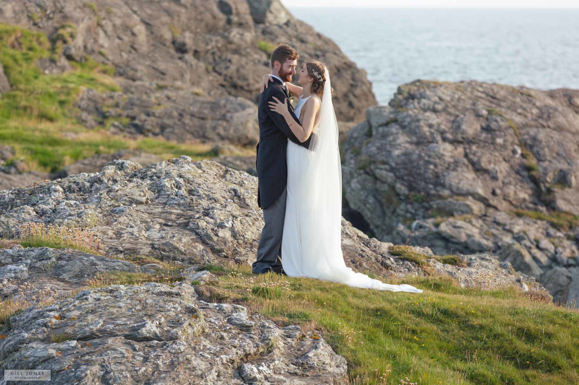a bride and groom hugging on the rocks in trearddur bay