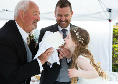 the bridesmaid takes a bite out of the wedding cake that her grandfather is holding by Anglesey photographer Gill Jones Photography
