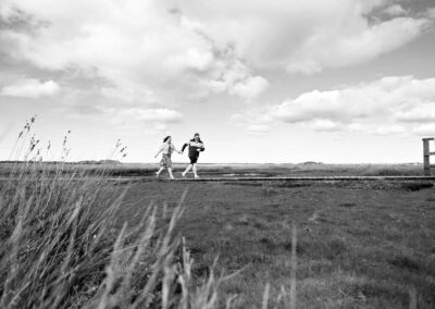 a couple run along a wooden walk way with big fluffy clouds in the sky by Anglesey wedding photographer Gill Jones Photography