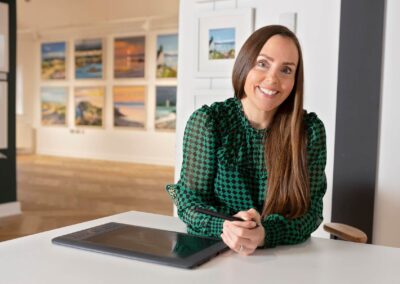 an artist holds a pen and tablet with her gallery in the background by Anglesey commercial photographer Gill Jones photography