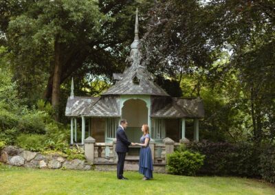 man and woman face eachother holding hands in front of an ornate summer house by Anglesey elopement photographer Gill Jones Photography