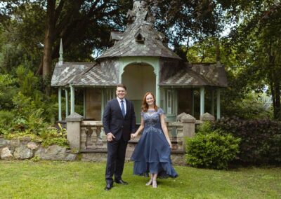 a man and a woman stand hand and hand infront of a summer house, they smile sweetly by Anglesey elopement photographer Gill Jones Photography