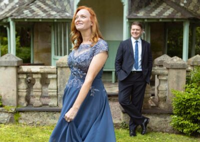 a woman wearing a blue dress swings the skirt whilst her husband stands behind her and smiles by Anglesey elopement photographer Gill Jones Photography