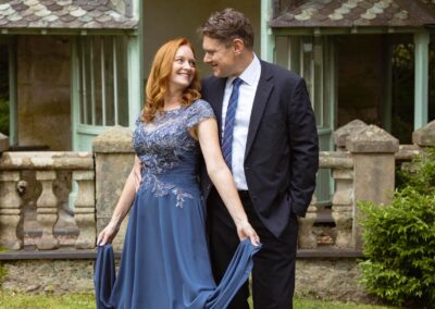 a woman wearing a chiffon blue dress turns towards her husband , they smile at one another by Anglesey elopement photographer Gill Jones Photography