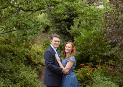 a couple caress whilst standing surrounded by a summer garden by Anglesey elopement photographer Gill Jones Photography