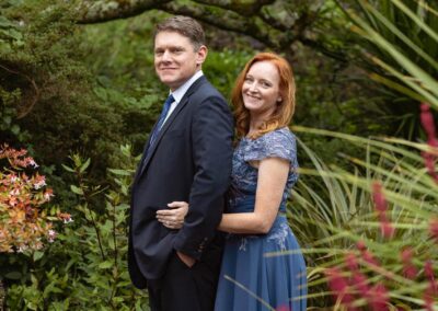 a man stands with his back to his wife, she holds him around the waist in a summer garden by Anglesey elopement photographer Gill Jones Photography