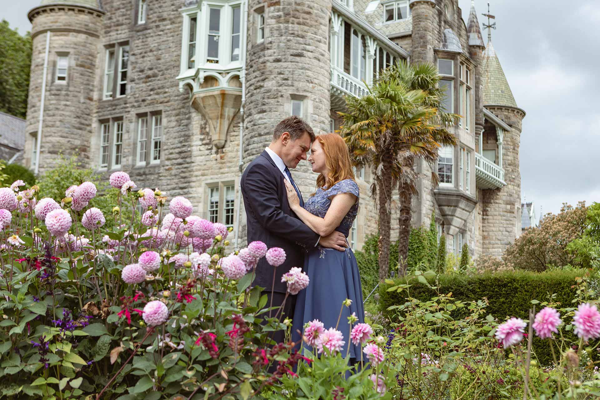 bride and groom face each other with foreheads touching amongst dahlias in the grounds of a chateau by Anglesey Photographer Gill Jones Photography