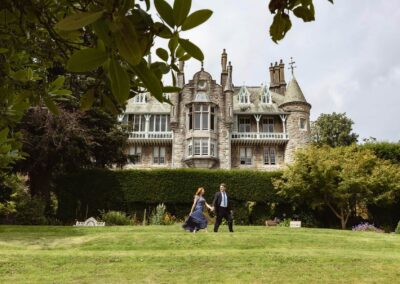 a husband and wife walk briskly hand in hand in front of a chateau by Anglesey elopement photographer Gill Jones Photography