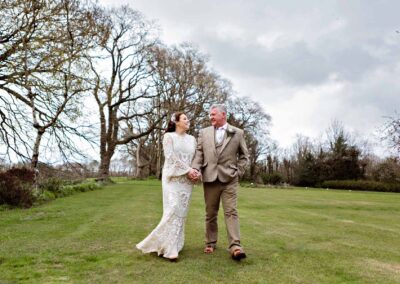 mature bride and groom walk towards Plas Dinas Country House with wintry trees in the background by Anglesey photographer Gill Jones Photography