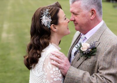 mature bride and groom gaze into eachothers eyes with noses almost touching his hand is on her shoulder by Anglesey photographer Gill Jones Photography