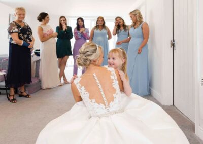 group of bridesmaids admire a bride as she hugs her daughter who has just seem her mum in her wedding dress