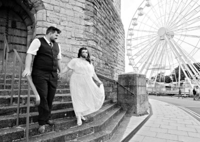 a bride and groom walk down the steps of a castle with a fair ground wheel to the side of them