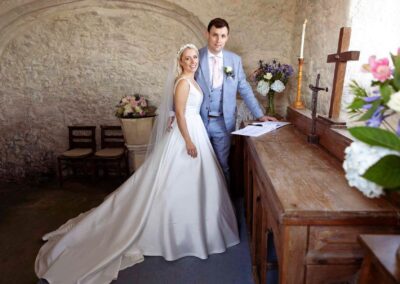 a bride and groom stand by a wooden table in an ancient church. They have just signed a register after being married.