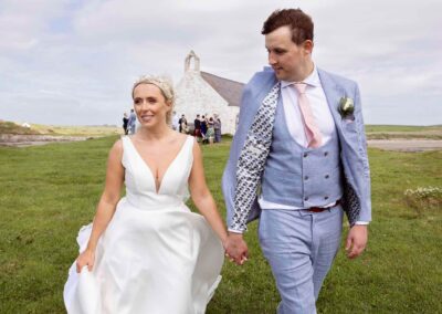 a bride and groom walk hand in hand with the wind in their hair