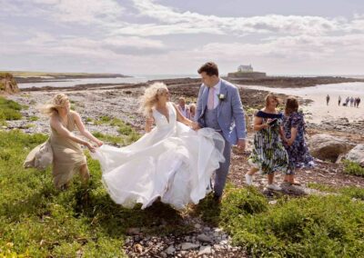 a bride and groom have walked across a causeway a bridesmaid holds the bride's dress so it doesn't drop to the floor