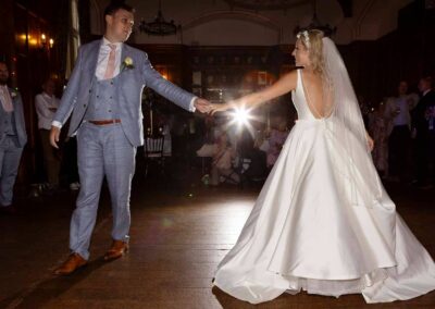 a bride and groom hold their arms out to touch finger tips, they'l begin their first dance on a dance floor any moment