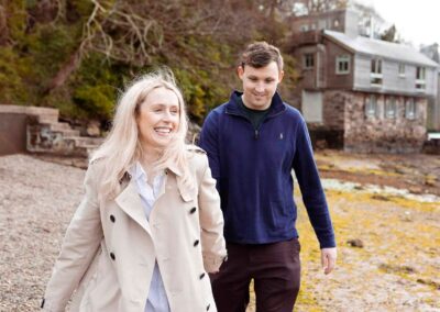 a woman walks ahead of her partner along a beach smiling broadly