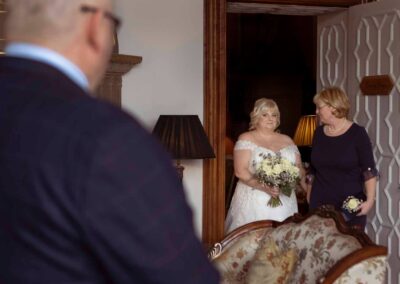 a bride walks through an open door with her sister before walking towards her groom