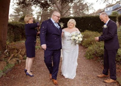 a bride and groom walk hand in hand just as confetti is thrown by their two friends