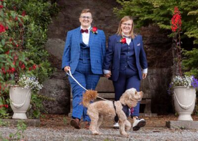 two women walk hand in hand one is holding the lead of their dog