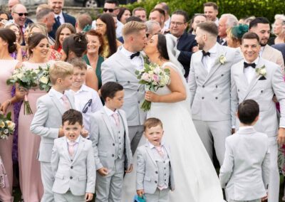 a group of wedding guests stand around the bride and groom as they kiss