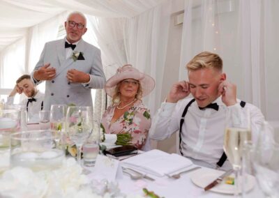 a groom holds his fingers in his ears as his father makes his speech