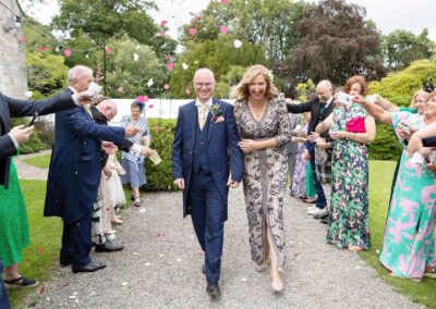 a couple of newly weds walk through an aisle as their friends throw confetti