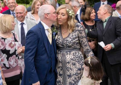 a groom goes to kiss his bride on her cheek a couple behind do the same to one another