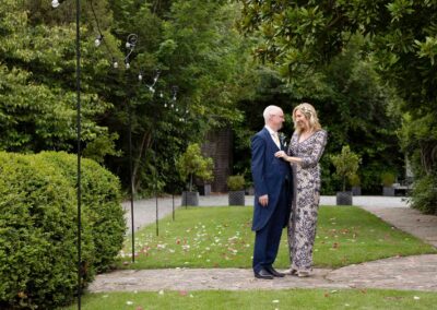 a bride and groom stand closely within a garden, she adjusts his jacket