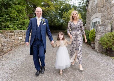 a bride and groom walk forward with their daughter between them holding hands