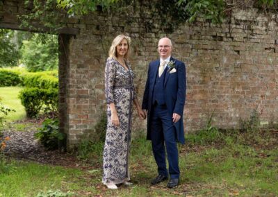 a bride and groom stand with finger tips touching an old brick garden wall is behind them