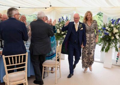 a bride and groom enter a marquee hand in hand, their guests clap