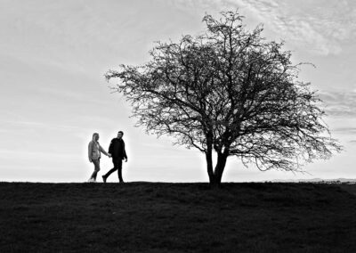 a silhouette of a man and woman walking towards a lone tree